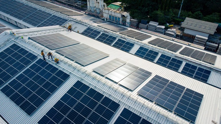 Workers installing solar panels on a large industrial rooftop with existing panels. - © Kay Dittner/Unsplash