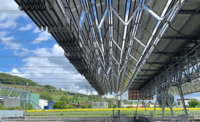 Solar panels arranged in a V-shape on a structure, with a scenic rural landscape and blue sky in the background. - © DHP Technology