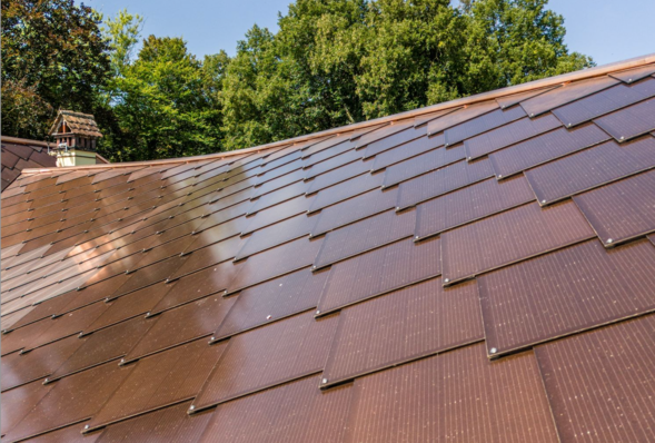 Roof with brown solar tiles against a backdrop of lush green trees under a clear blue sky. - © Sunstyle