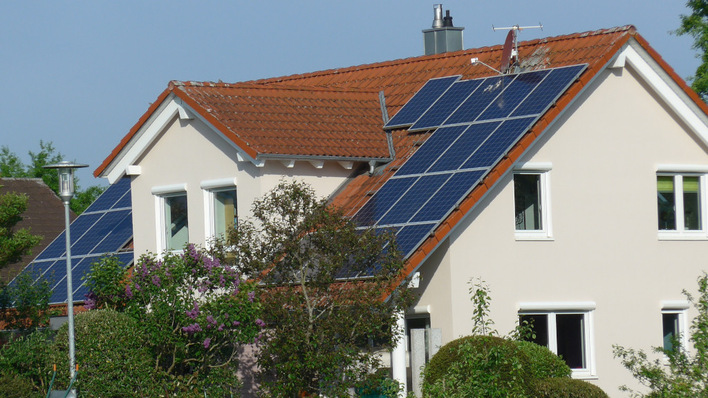 Ein Haus mit roten Dachziegeln und installierten Sonnenkollektoren, umgeben von Bäumen und Sträuchern. - © Hans-Christoph Neidlein Residential rooftop installation in southern Germany – even for small PV systems, the internet can be a gateway for cyber attacks.