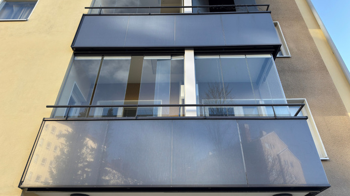 Blick auf die Fassade eines modernen Wohnhauses mit Glasbalkonen, in denen sich der Himmel und die umliegenden Gebäude spiegeln. - © Lumon Deutschland To the casual observer, the balcony appears ordinary despite its energy function